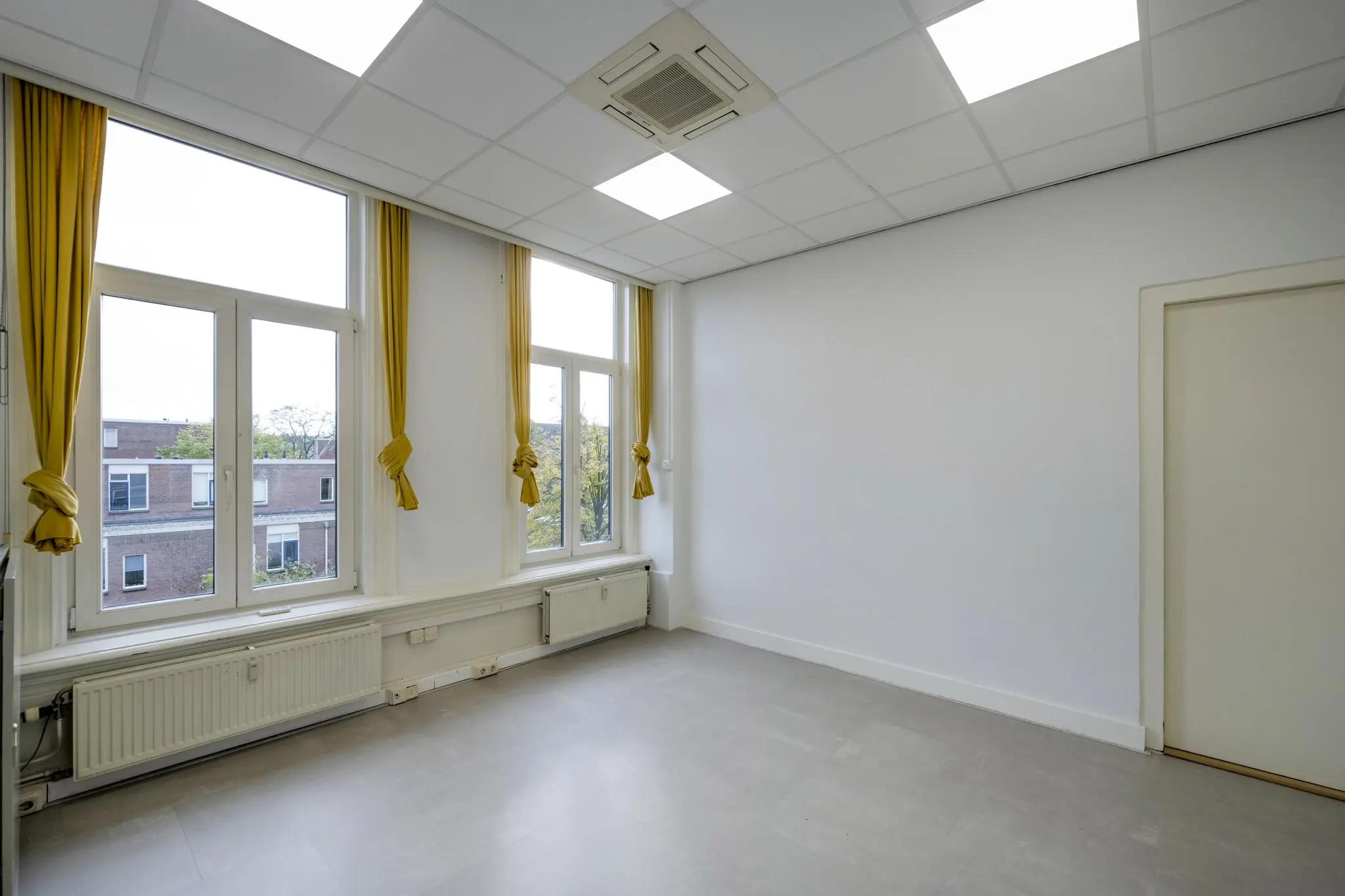 Lichte, lege kamer aan de Nieuwe Gracht met grote ramen, gele gordijnen en plafondverlichting.